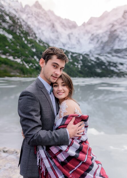 Dreamy honeymoon of just married couple in love in the winter mountains and picturesque frozen lake