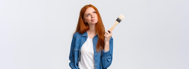 Free photo dreamy and indecisive cute redhead female in denim shirt smirk and squinting thoughtful looking up i