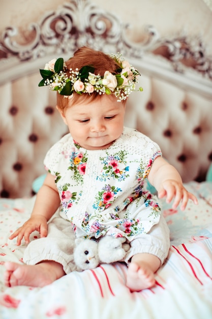 Dreamy little girl in rose wreath sits on soft luxury bed