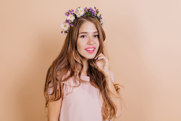 Foto gratuita donna bruna dai capelli lunghi sognante con fiori viola nei capelli che sorride alla macchina fotografica