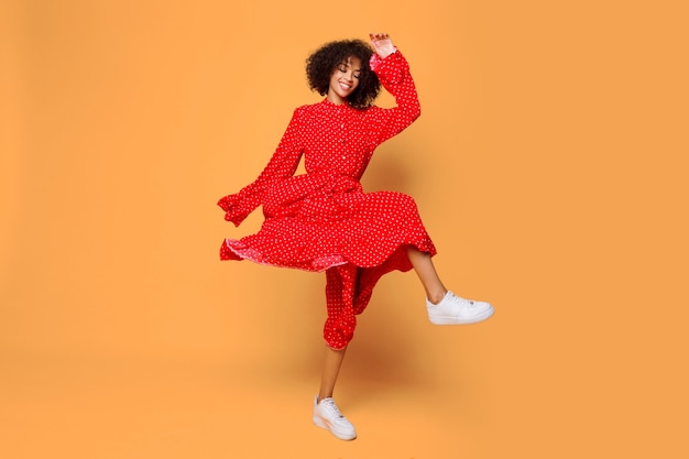 Бесплатное фото Мечтательное настроение. стильная африканская девушка танцует и прыгает на апельсине