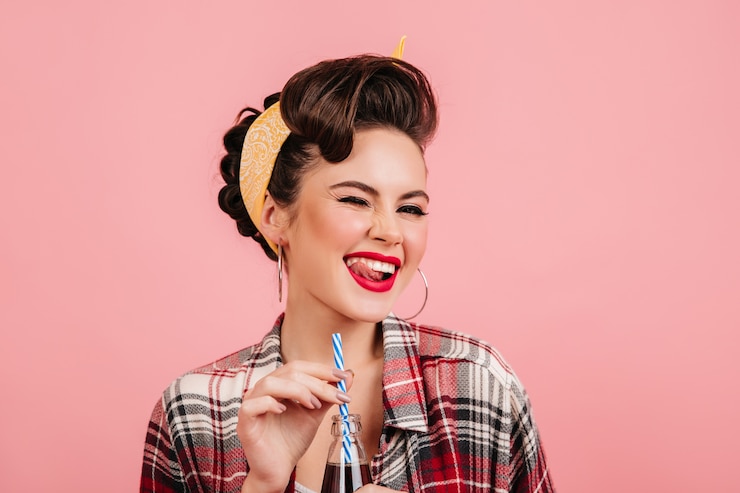 Free Photo dreamy pinup girl with bright makeup laughing on pink background. studio shot of carefree lady drinking beverage.