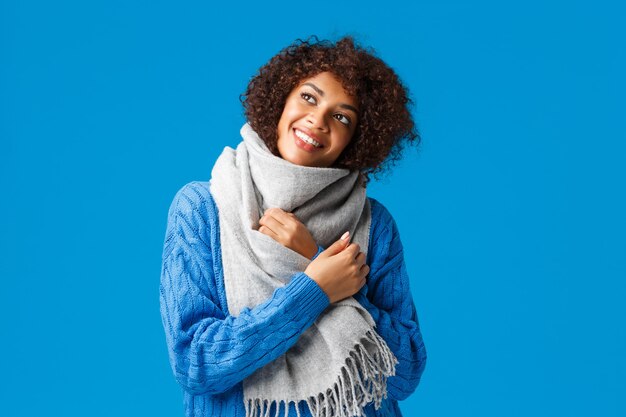 Dreamy romantic and carefree african american woman in winter sweater, scarf, looking up thoughtful,blue wall