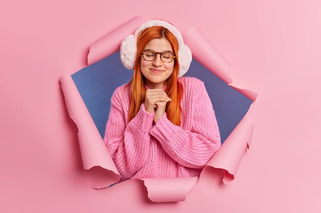 Dreamy satisfied redhead young Caucasian woman keeps hands pressed together.