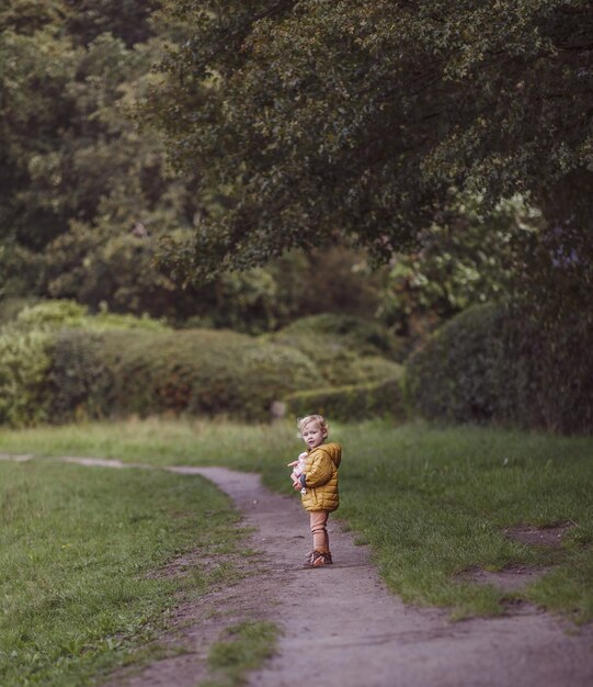 Dreamy shot of an adorable Caucasian toddler girl standing on a footpath in a countryside