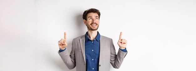 Free photo dreamy smiling male manager in suit pointing and looking up happy face checking out advertisement st