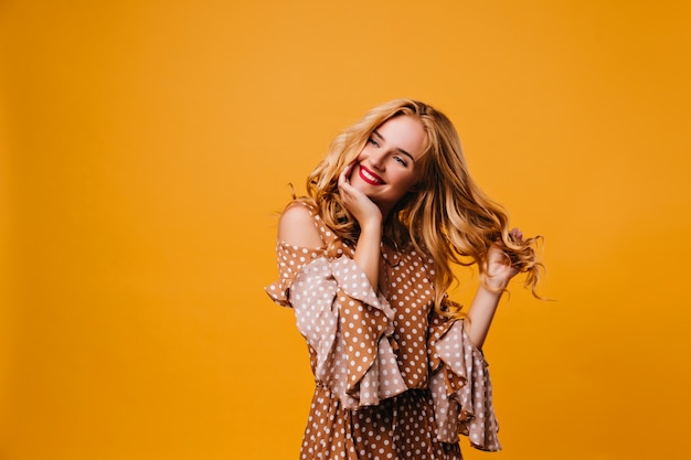 Dreamy smiling woman playing with her hair.  amazing caucasian lady with red lips laughing on yellow wall.