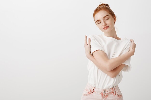 Dreamy tender redhead woman embracing own body with closed eyes