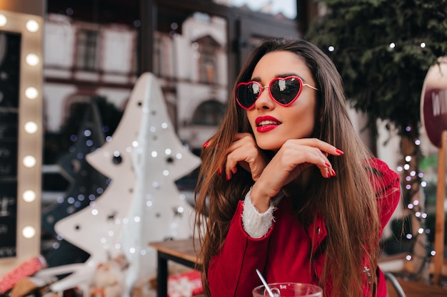 Free photo dreamy white woman in trendy heart sunglasses chilling in cafe