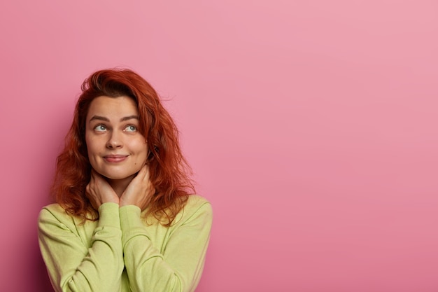 dreamy woman in love recalls perfect date with boyfriend, thinks about cute sweet things, keeps hands on neck, looks somewhere, wears green sweater