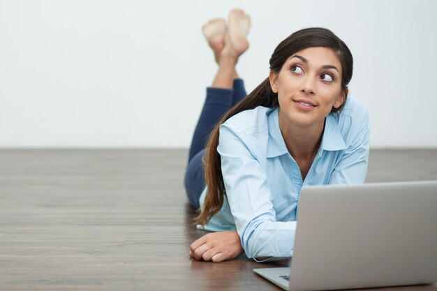 Dreamy Woman Lying on Floor and Working on Laptop