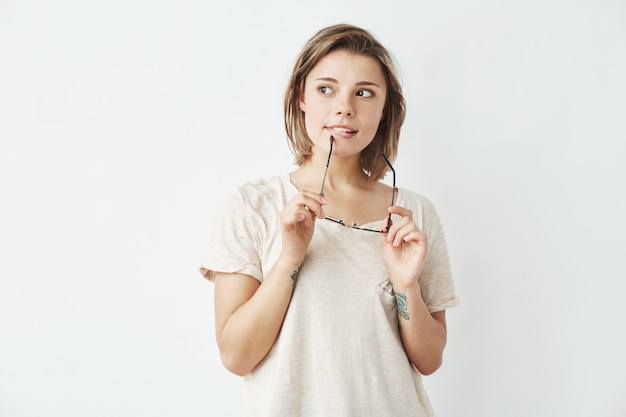 Dreamy young beautiful girl looking in side thinking holding glasses .