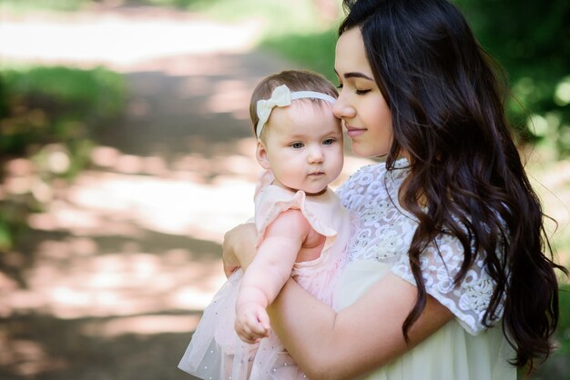 Dreamy young mommy holds her little daughter posing outside