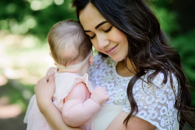 Dreamy young mommy holds her little daughter posing outside