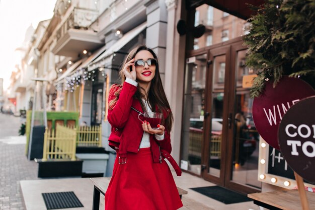 Dreamy young woman touching her black sunglasses while walking down the street