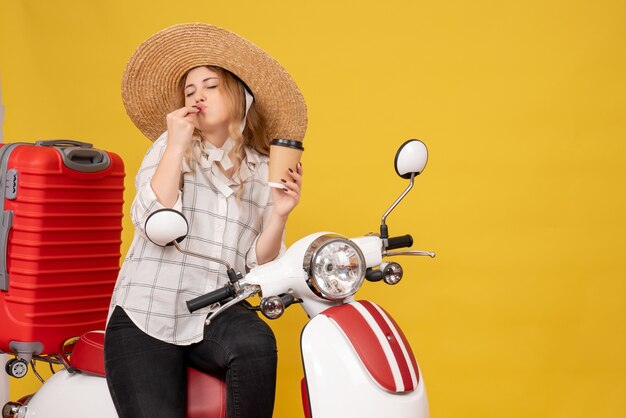 Dreamy young woman wearing hat and sitting on motorcycle and showing ticket