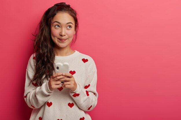 Dremay pleasant looking teenage girl with pony tail, wears casual jumper, uses mobile phone