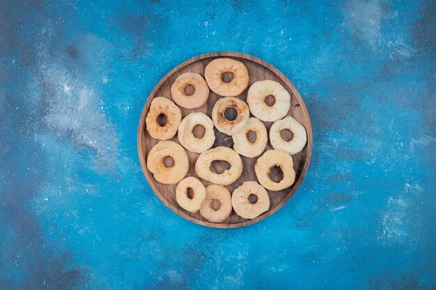 Dried apple chips on wooden plate on blue surface