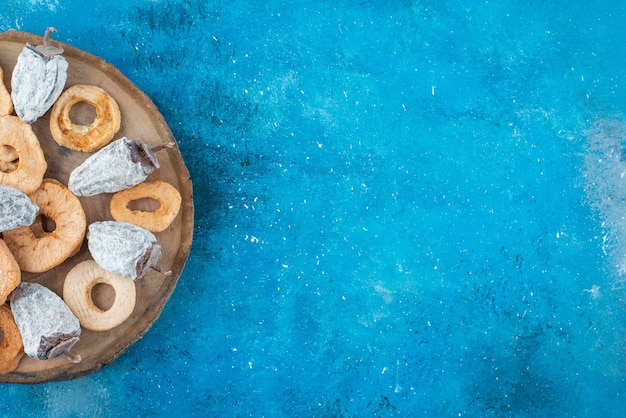 Free photo dried apple rings and persimmon on a board on the blue surface