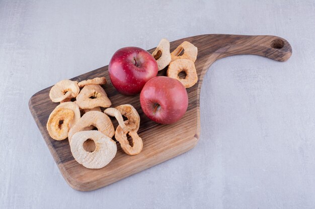 白い背景の上の木の板に乾燥したリンゴのスライスとリンゴ全体。