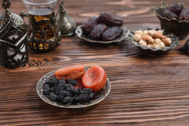 Dried apricot and black raisin on metallic plate on wooden textured backdrop