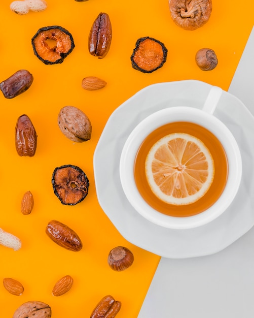 Dried apricot; dates; almonds; walnut; peanut and hazelnut with lemon tea cup on yellow and white backdrop