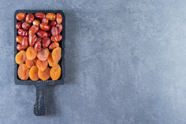 Dried apricot and oleaster on a board, on the marble background.