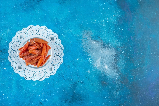 Dried apricots in a bowl on coaster on the blue surface