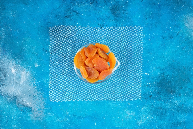 Dried apricots in a glass bowl , on the blue table. 