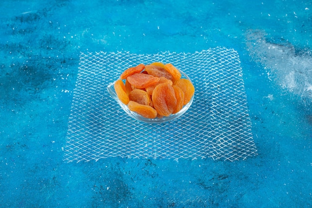 Бесплатное фото Сушеные абрикосы в стеклянной миске, на синем столе.