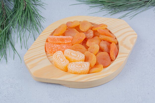 Dried apricots and marmalade candies on wooden plate. 