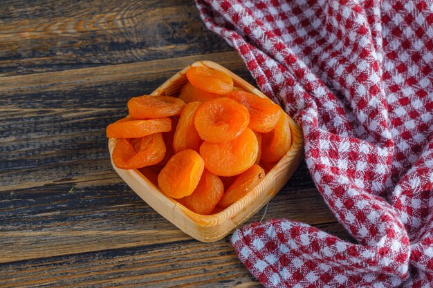 Dried apricots in a wooden plate on wooden and picnic cloth. .