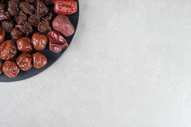 Dried black and brown plums on a wooden platter.