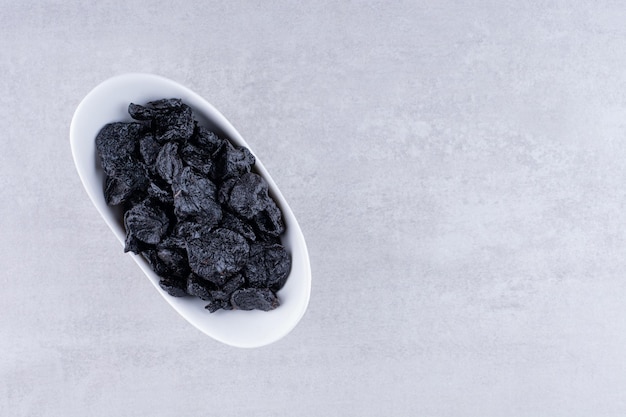 Dried black sultanas in a plate on concrete background. High quality photo