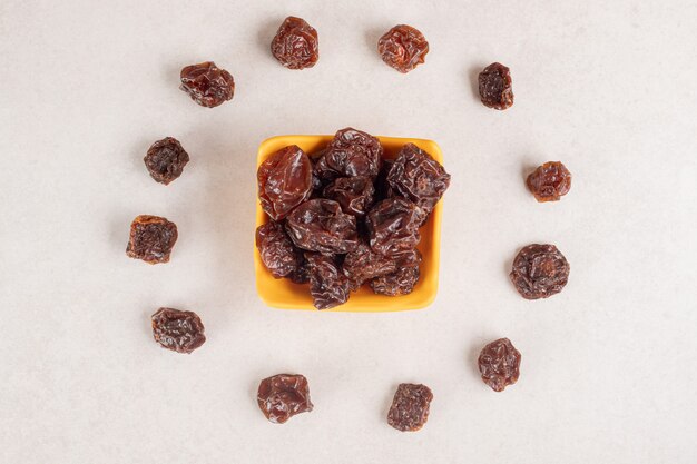 Dried brown plums in a ceramic cup or bowl.