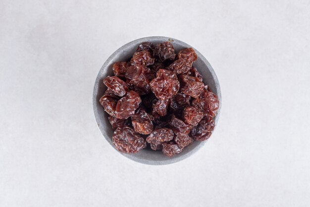 Dried brown plums in a ceramic cup or bowl.