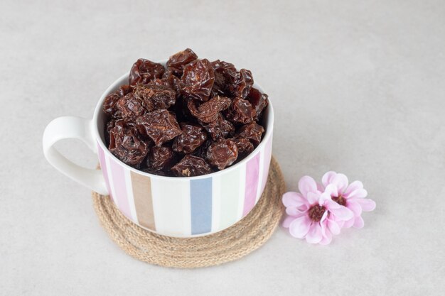 Dried brown plums in a ceramic cup.