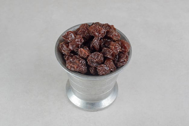 Dried brown plums in a metallic cup.