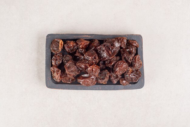 Dried brown plums on a wooden platter.