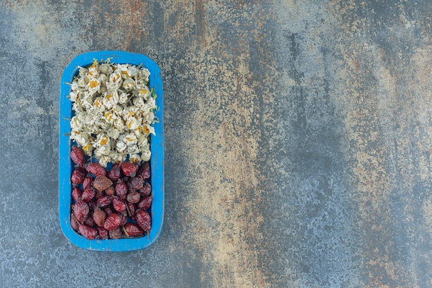 Сушеные ромашки и плоды шиповника на синей тарелке.