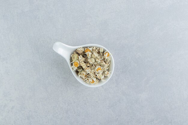 Dried chamomile flowers in white bowl.  