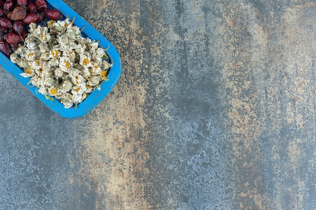 Free photo dried chamomile and rosehips on blue plate.