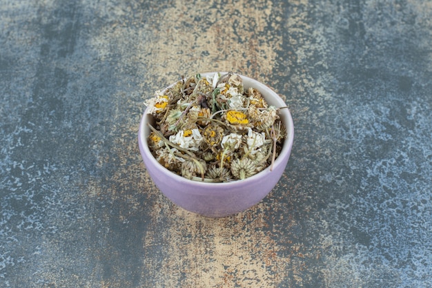 Free photo dried chamomile tea in purple bowl.