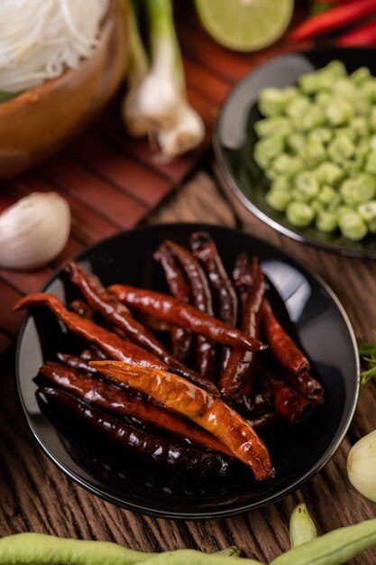 Dried chilies fried in a black plate with lentils. Cucumbers and garlic are placed on the wooden table