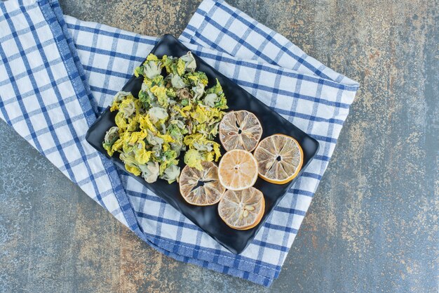 Dried chrysanthemum and lemon slices on black plate.