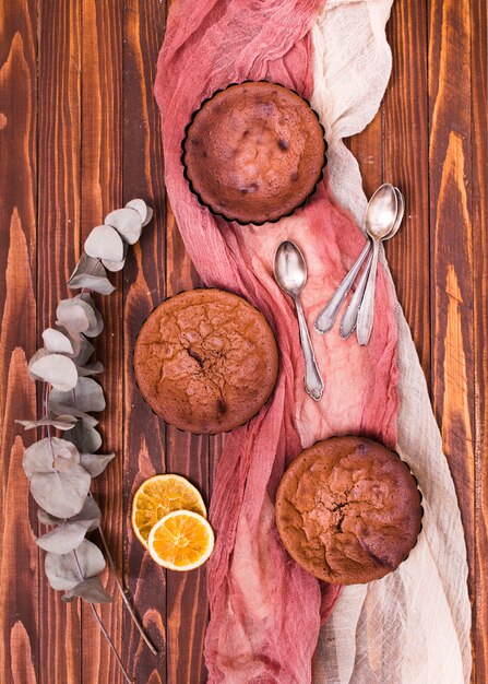 Dried eucalyptus populus leaves and citrus slices with three baked cake and spoons on linen clothes over the wooden table