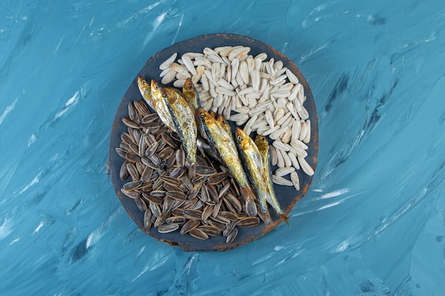 Free photo dried fish and kernel on a board , on the blue surface.