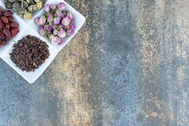 Dried flowers, rosehips and cloves on white plate.