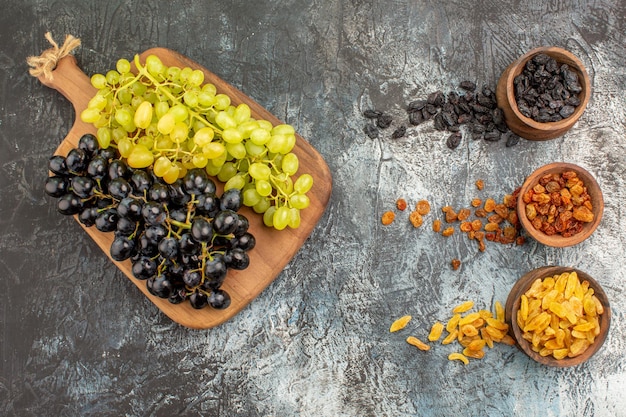 Free photo dried fruits bunches of green and black grapes on the board and dried fruits