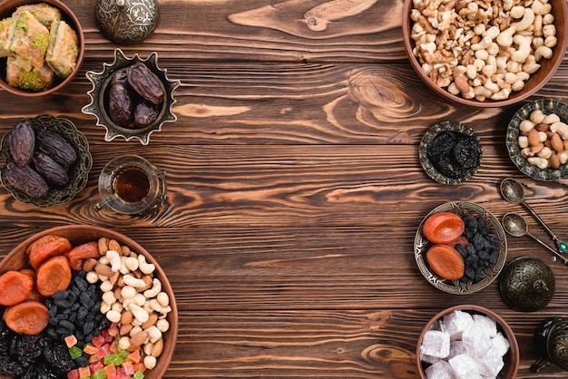 Dried fruits; nuts; dates and lukum on earthen and metallic bowls on wooden desk